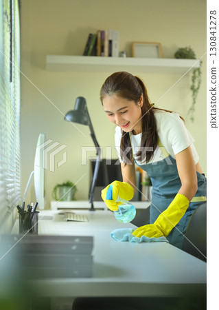 Smiling woman disinfecting desk with spray cleaner and cloth in office, concept of hygiene and sanitation Smiling woman disinfecting desk with spray cleaner and cloth in office, concept of hygiene and sanitation 130841278
