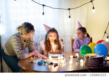 Joyful birthday celebration with friends and family around a cake decorated with candles, colorful balloons, and festive lights in a cozy indoor setting during the evening Joyful birthday celebration with friends and family around a cake decorated with candles, colorful balloons, and festive lights in a cozy indoor setting during the evening 130841372