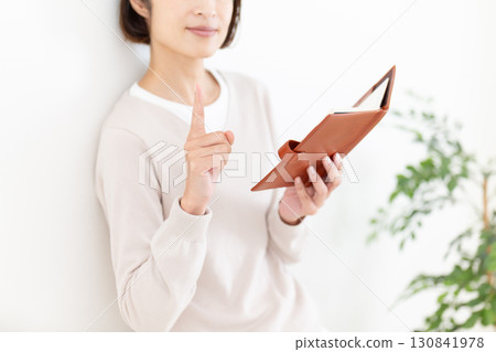 一位穿著休閒服的中年婦女拿著筆記本,食指向上 一位穿著休閒服的中年婦女拿著筆記本,食指向上 130841978