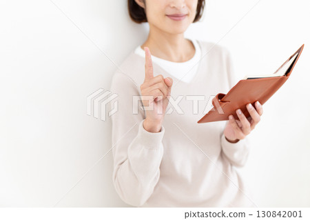 一位穿著休閒服的中年婦女拿著筆記本，食指向上 130842001
