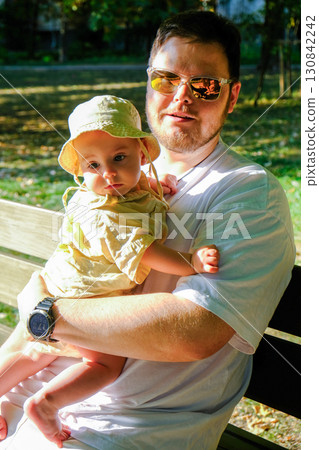 Man with Baby in Sun Hat on Park Bench 130842242