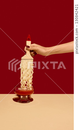 Hand holding paintbrush dipped in tomato sauce with spaghetti strands on red background Hand holding paintbrush dipped in tomato sauce with spaghetti strands on red background 130842421