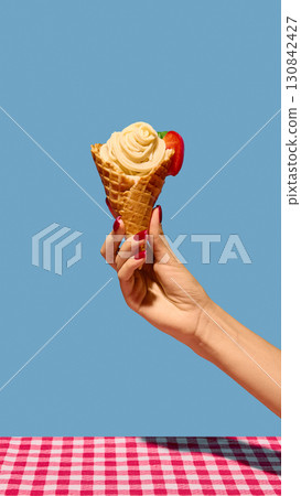 Female hand with red nails holding waffle cone filled with spaghetti and tomato as dessert 130842427