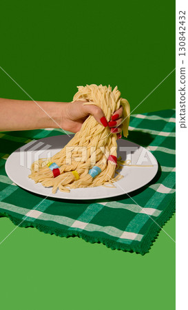 Hand with red nails holding braided spaghetti strands with colorful bands on white plate 130842432