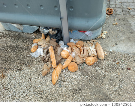 Soggy bread and baguettes fill the ground near a grocery store dumpster, left uncollected. The area shows signs of rain, emphasizing food waste and improper disposal. Soggy bread and baguettes fill the ground near a grocery store dumpster, left uncollected. The area shows signs of rain, emphasizing food waste and improper disposal. 130842501