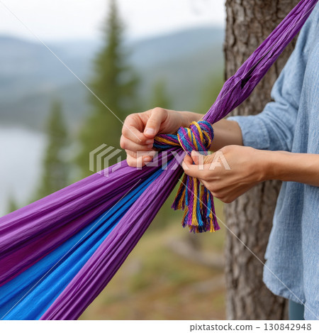 Colorful hammock tied to tree with hands outdoors in nature with blurred forest background Colorful hammock tied to tree with hands outdoors in nature with blurred forest background 130842948