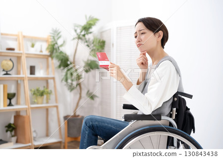 一位坐在輪椅上的女人拿著智慧型手機和一張卡片 一位坐在輪椅上的女人拿著智慧型手機和一張卡片 130843438