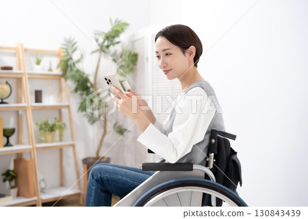 一位坐在輪椅上的女人拿著智慧型手機和一張卡片 130843439