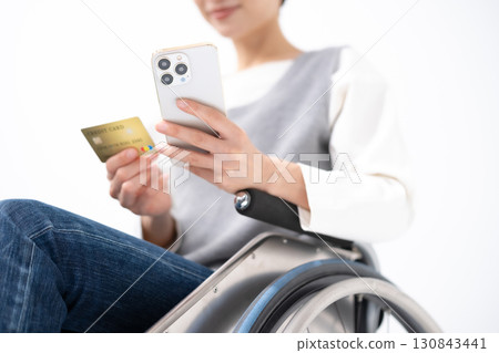 一位坐在輪椅上的女人拿著智慧型手機和一張卡片 一位坐在輪椅上的女人拿著智慧型手機和一張卡片 130843441