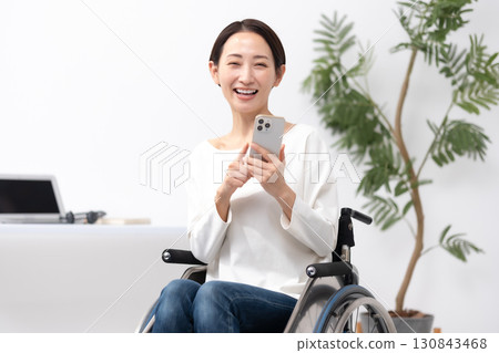 Woman in wheelchair working from home smartphone Woman in wheelchair working from home smartphone 130843468