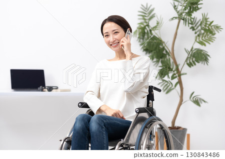 坐在輪椅上的女人在家工作，打電話 130843486