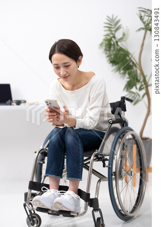 Woman in wheelchair working from home smartphone 130843491