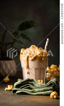 Creamy caramel milkshake topped with popcorn and served in a glass with a straw Creamy caramel milkshake topped with popcorn and served in a glass with a straw 130843598