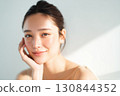 A Japanese woman in front of a white wall with natural light reflecting beautifully on her bare skin 130844352