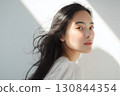 A Japanese woman in front of a white wall with natural light reflecting beautifully on her bare skin 130844354