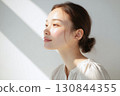 A Japanese woman in front of a white wall with natural light reflecting beautifully on her bare skin 130844355