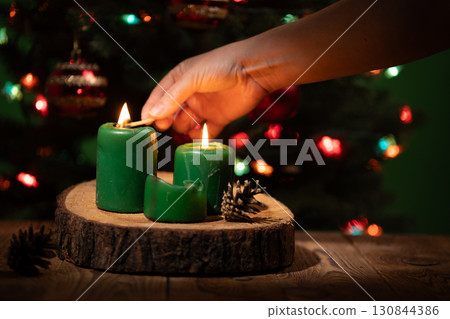 Hand Lighting Green Christmas Candles on a Wooden Surface 130844386