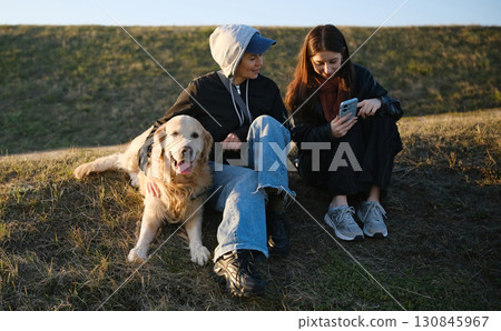 Mother And Daughter Relaxing Outdoors With Golden Retriever Sitting On The Grass Mother And Daughter Relaxing Outdoors With Golden Retriever Sitting On The Grass 130845967