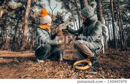 Mother And Little Daughter Walk With Golden Retriever In An Autumn Park, Playing And Asking The Dog To Give A Paw 130845970