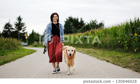 Smiling Girl Walks With Golden Retriever, A Dog Of The Golden Retriever Breed 130846028