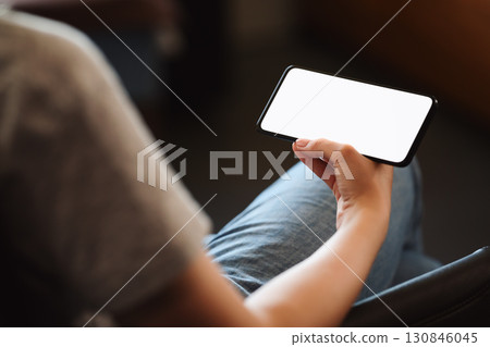Young woman hold smarphone with white screen while sitting in a chair Young woman hold smarphone with white screen while sitting in a chair 130846045