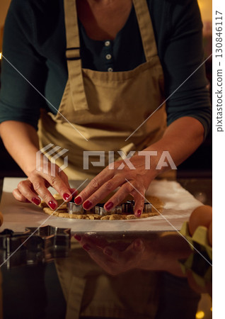 Woman Preparing Gingerbread Cookies with Festive Lights in Warm Kitchen Setting 130846117