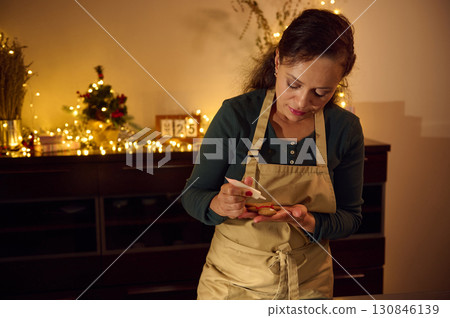 Festive Woman Preparing Holiday Gingerbread Cookies in Warm Christmas Setting 130846139