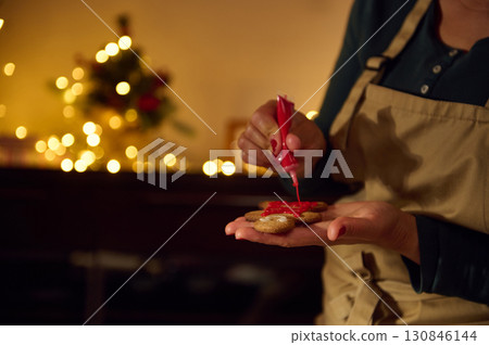 Woman Decorating Holiday Cookies with Red Icing Amidst Christmas Lights Woman Decorating Holiday Cookies with Red Icing Amidst Christmas Lights 130846144