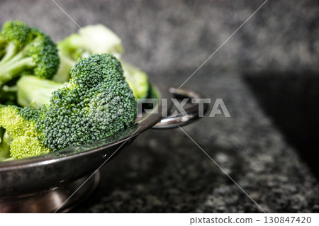 Fresh broccoli in a metal colander on kitchen counter Fresh broccoli in a metal colander on kitchen counter 130847420