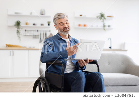 Mature Caucasian man in wheelchair having video call at home, engaging with communication. Technology promotes inclusivity and interaction for professional or personal connections using laptops. Mature Caucasian man in wheelchair having video call at home, engaging with communication. Technology promotes inclusivity and interaction for professional or personal connections using laptops. 130847613