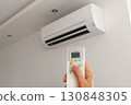 Air conditioner temperature adjustment with remote controller in room at home. Hand holding remote controller of air conditioner inside the white room and set at cool temperature 130848305