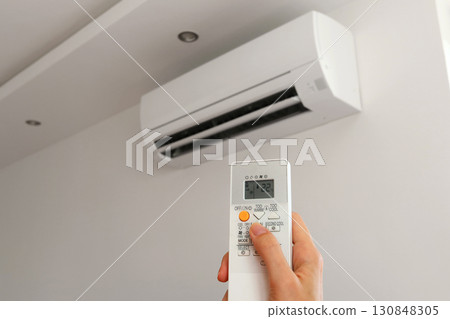 Air conditioner temperature adjustment with remote controller in room at home. Hand holding remote controller of air conditioner inside the white room and set at cool temperature 130848305