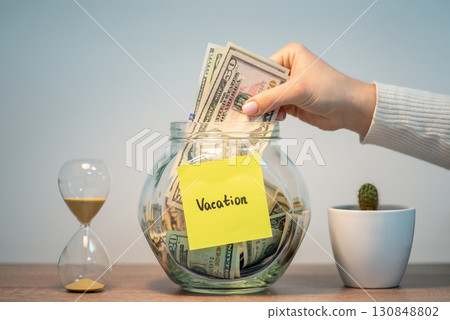 Female hand putting stack of dollars in glass jar with inscription Vacation. Savings for travel, holidays concept 130848802