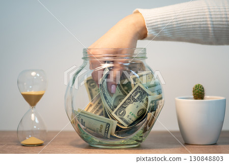 Hand taking money out of glass bank. Saving money concept, buying something 130848803