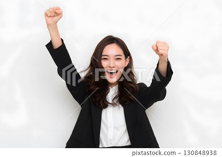 A joyful young woman smiles brightly, raising her clenched fists high, celebrating immense success and personal achievement. A joyful young woman smiles brightly, raising her clenched fists high, celebrating immense success and personal achievement. 130848938