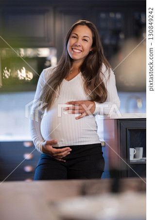 Smiling pregnant woman standing in modern kitchen with positive energy Smiling pregnant woman standing in modern kitchen with positive energy 130849242