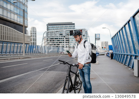 City commuter riding bike from work, reading text message on phone. 130849578