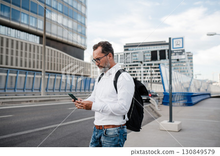 Mature businessman walking home from work, texting on smartphone. Mature businessman walking home from work, texting on smartphone. 130849579