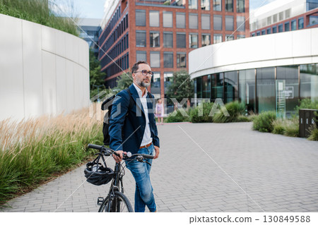 City commuter walking with bike to office, wearing backpack. 130849588
