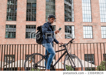 City commuter riding bike from work, reading text message on phone. 130849634