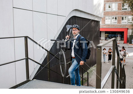 City commuter carrying bicycle up urban stairs. 130849636