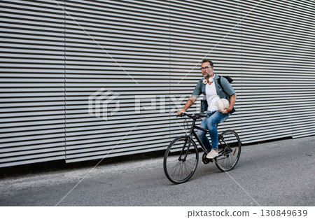City commuter riding bike on street, wearing backpack. 130849639