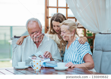 Senior couple showing family photo album to granddaughter. 130849682