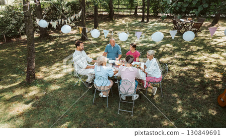 Areal view of grandparents, parents and kids dining together outside. Areal view of grandparents, parents and kids dining together outside. 130849691