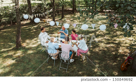 Areal view of grandparents, parents and kids dining together outside. Areal view of grandparents, parents and kids dining together outside. 130849692