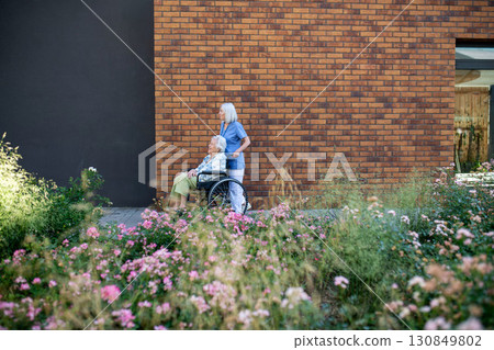 Side view of nurse pushing senior woman in wheelchair. Side view of nurse pushing senior woman in wheelchair. 130849802