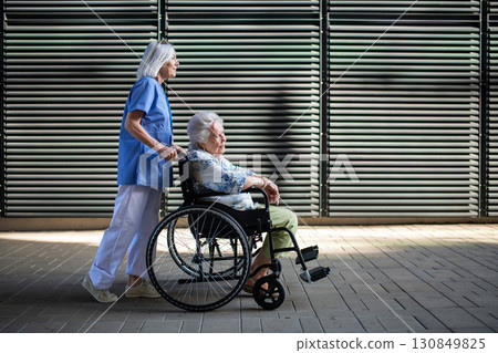 Side view of nurse pushing senior woman in wheelchair. Side view of nurse pushing senior woman in wheelchair. 130849825