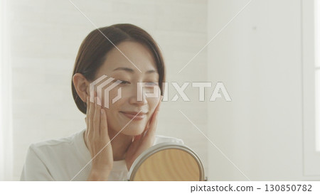 Middle-aged woman checking her skin condition in the mirror Middle-aged woman checking her skin condition in the mirror 130850782