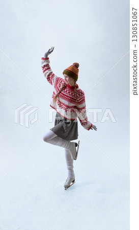 Girl figure skater in red winter sweater balancing on one leg with joy 130851067