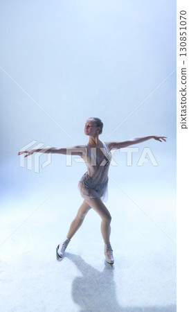 Graceful figure skater extending arms in balanced pose under soft light 130851070